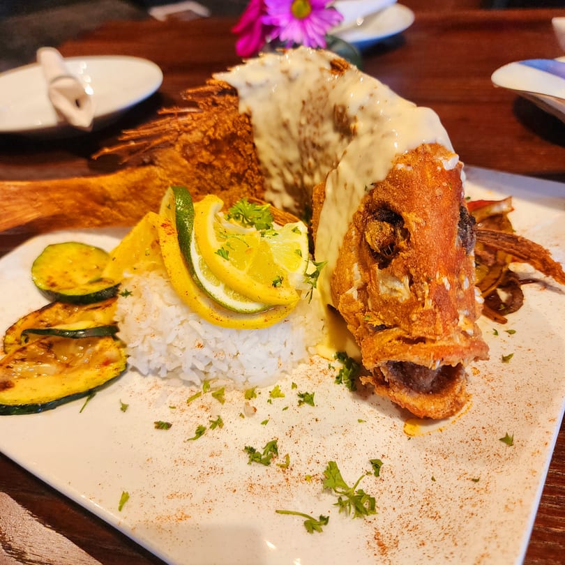 Crispy fried whole fish with creamy sauce, rice, grilled zucchini, and citrus slices.