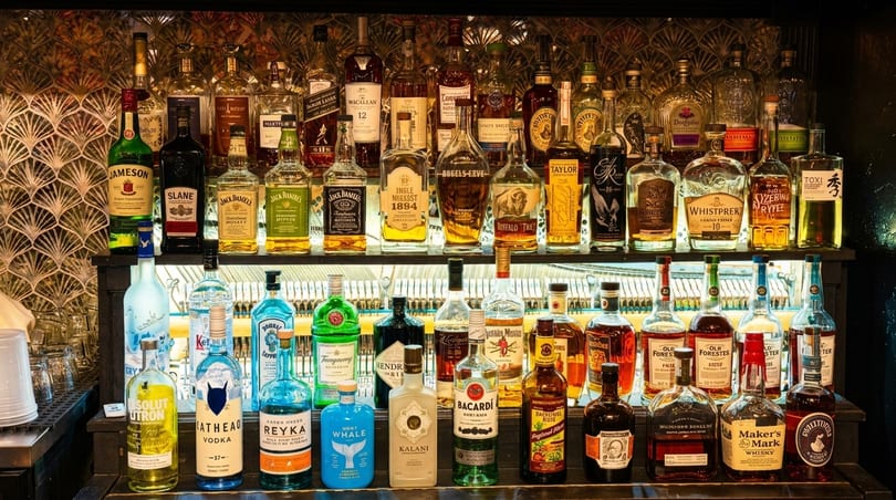 A well-stocked bar with two shelves of various liquor bottles, brightly lit from below.