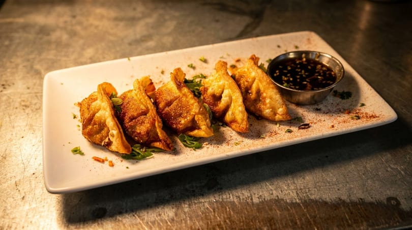 Crispy fried dumplings with a side of soy dipping sauce on a white rectangular plate.