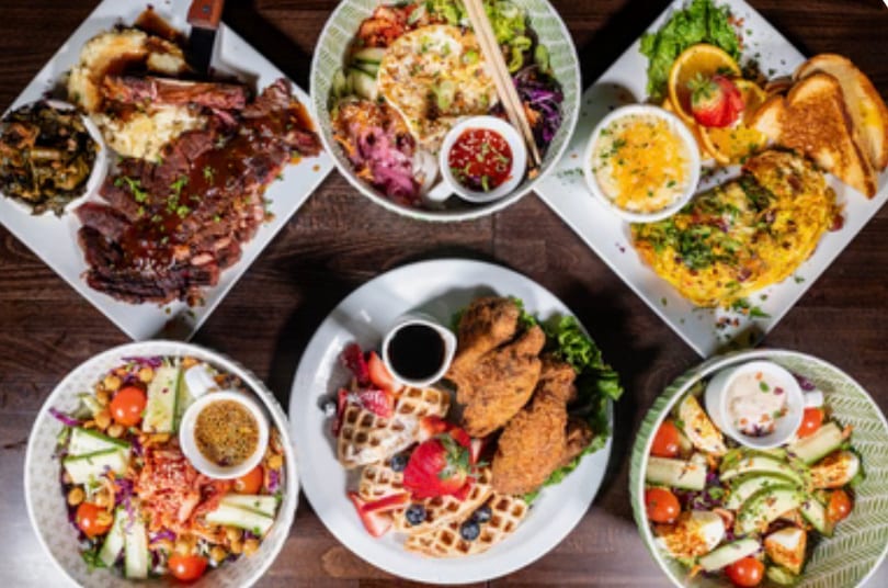 A diverse spread of restaurant dishes including steak, salads, omelet, and chicken and waffles.
